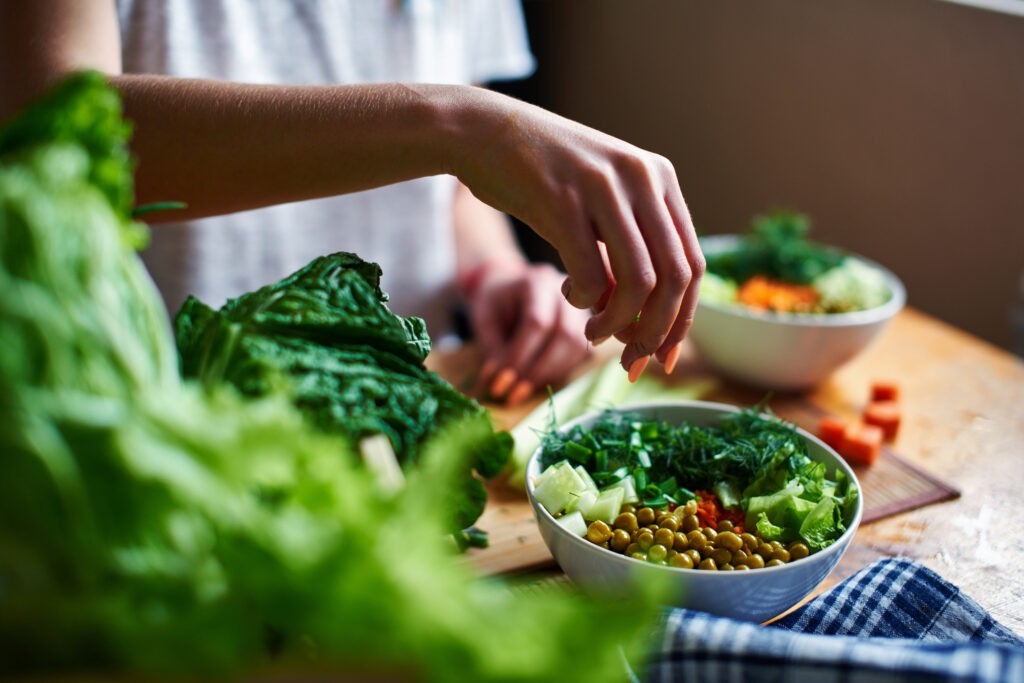 Female hand pours green onions in a bowl with green peas, cucumbers, carrots, lettuce and dill standing on a table Fibre solubili o insolubili