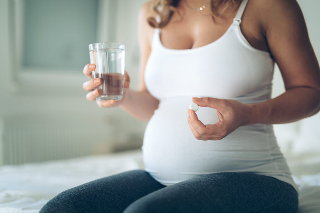 Donna incinta con un bicchiere e una pillola in mano